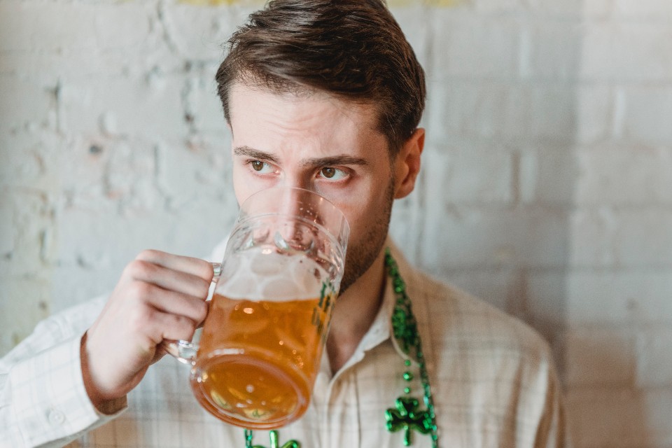 a man drinking a beer wearing a beaded necklace