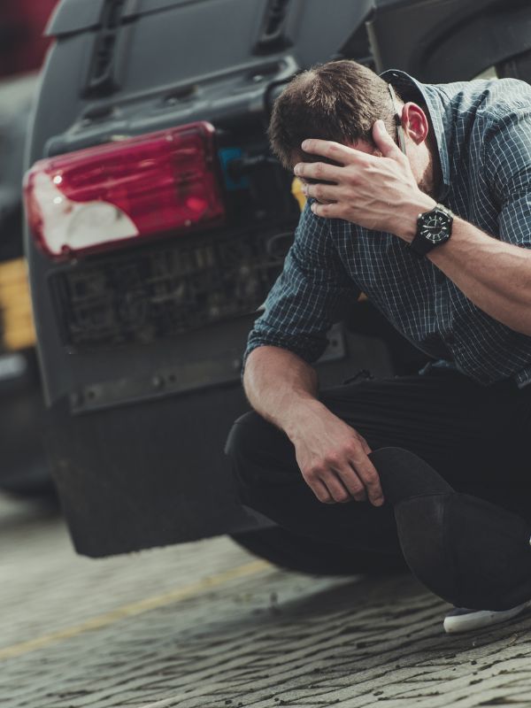 A man kneeling down holding his head after a DUI accident that resulted in a death.